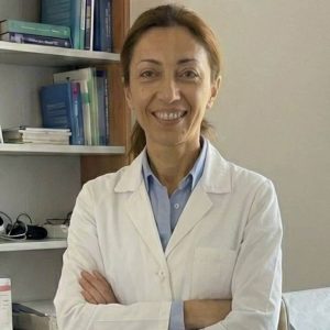 Donna professionista in laboratorio di erboristeria con libri e piante sullo sfondo.