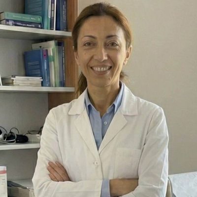 Donna professionista in laboratorio di erboristeria con libri e piante sullo sfondo.