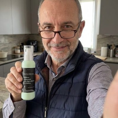 Uomo con barba e occhiali che mostra un prodotto naturale in cucina.